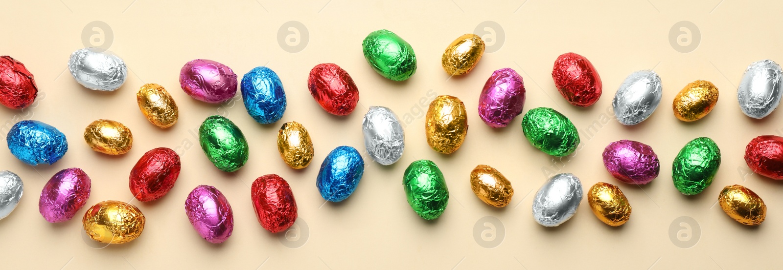 Image of Chocolate eggs wrapped in colorful foil on beige background, flat lay. Banner design