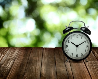 Image of Black alarm clock on wooden table, space for text. Daylight saving time (Spring forward)