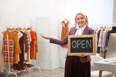Photo of Female business owner holding OPEN sign in boutique