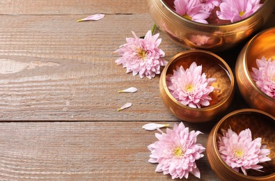 Photo of Tibetan singing bowls with water and beautiful flowers on wooden table, above view. Space for text