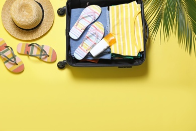Photo of Open suitcase and beach accessories on yellow background, flat lay. Space for text
