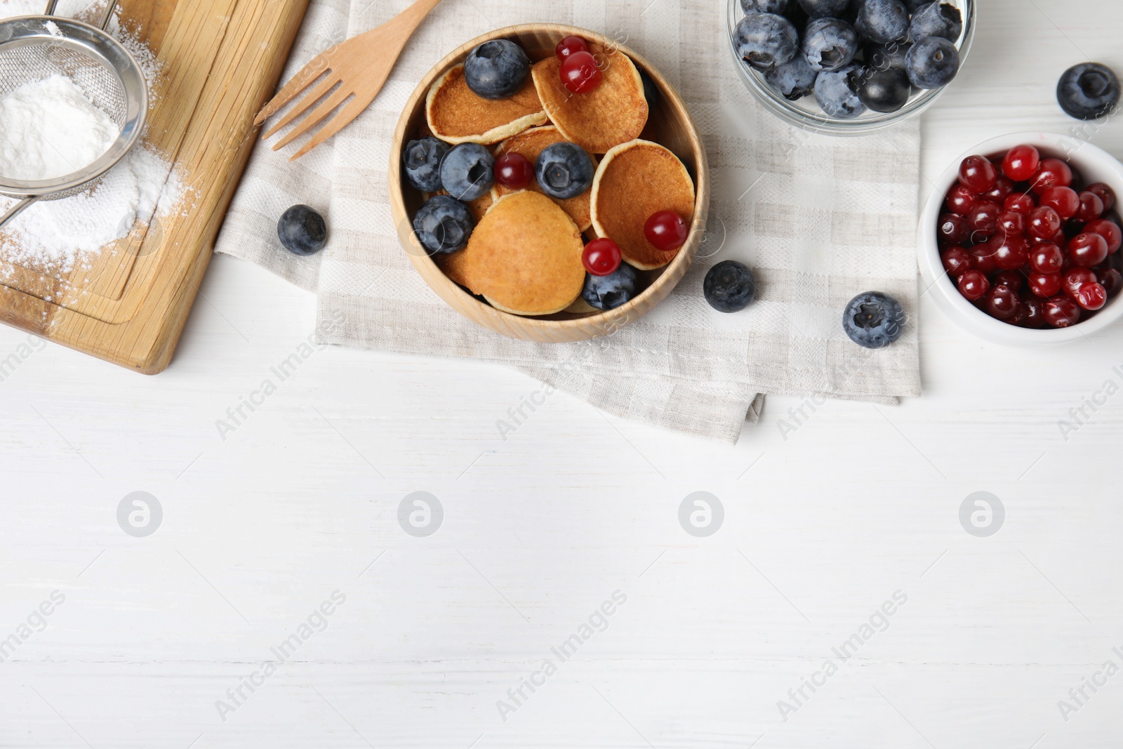 Photo of Delicious mini pancakes cereal with berries served on white table, flat lay. Space for text