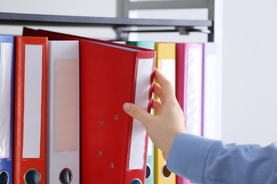 Woman taking folder with documents from shelf in office, closeup