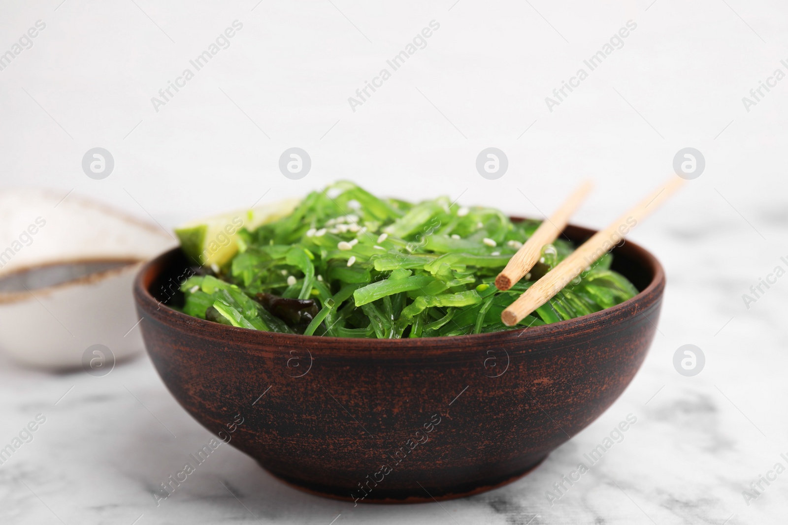 Photo of Tasty seaweed salad in bowl served on white marble table, closeup