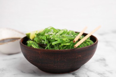 Photo of Tasty seaweed salad in bowl served on white marble table, closeup