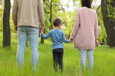 Photo of Little child holding hands with his parents in park. Family weekend