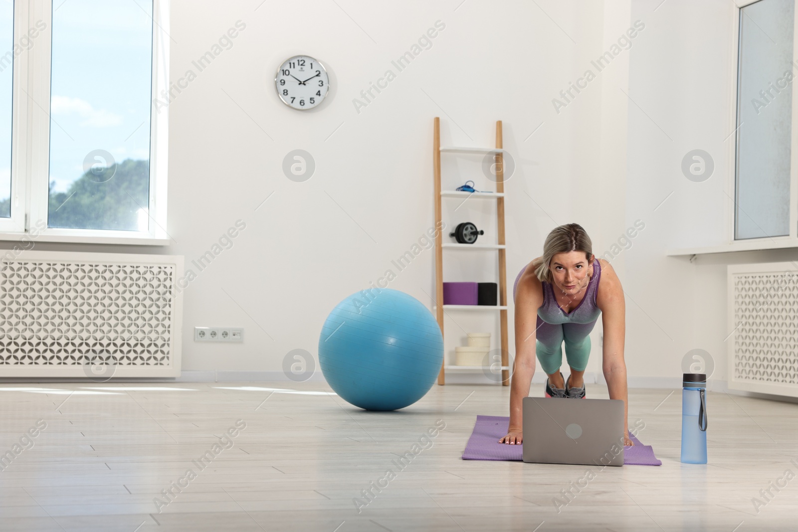 Photo of Online fitness trainer. Woman doing exercise near laptop at home