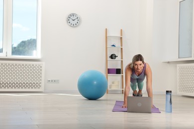 Online fitness trainer. Woman doing exercise near laptop at home