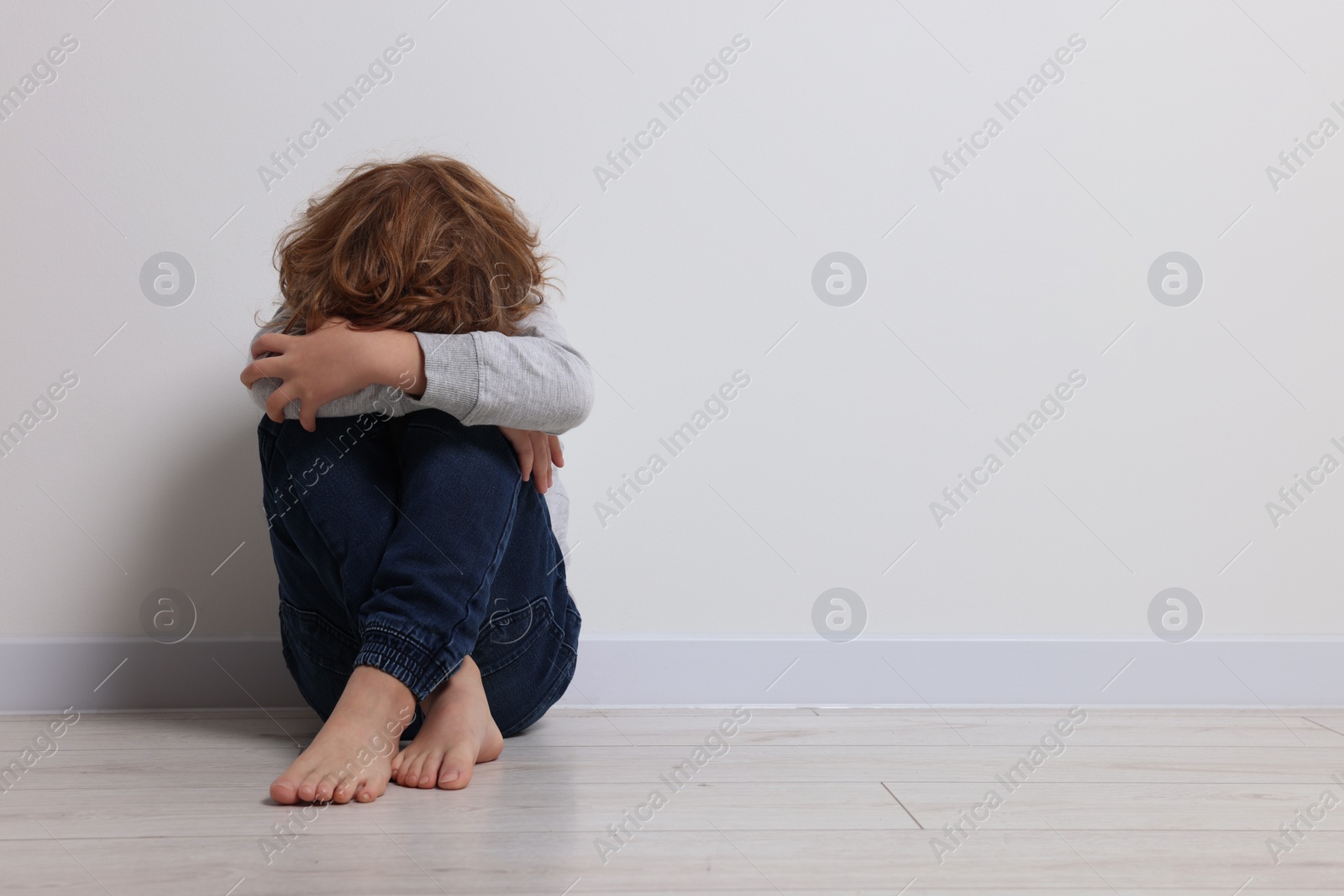 Photo of Child abuse. Upset boy sitting on floor near white wall, space for text