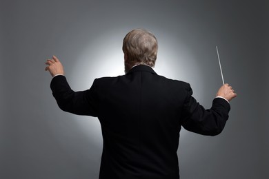 Professional conductor with baton on grey background, back view