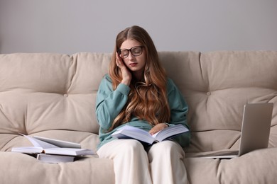 Young tired woman studying on couch indoors