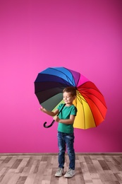 Little boy with rainbow umbrella near color wall