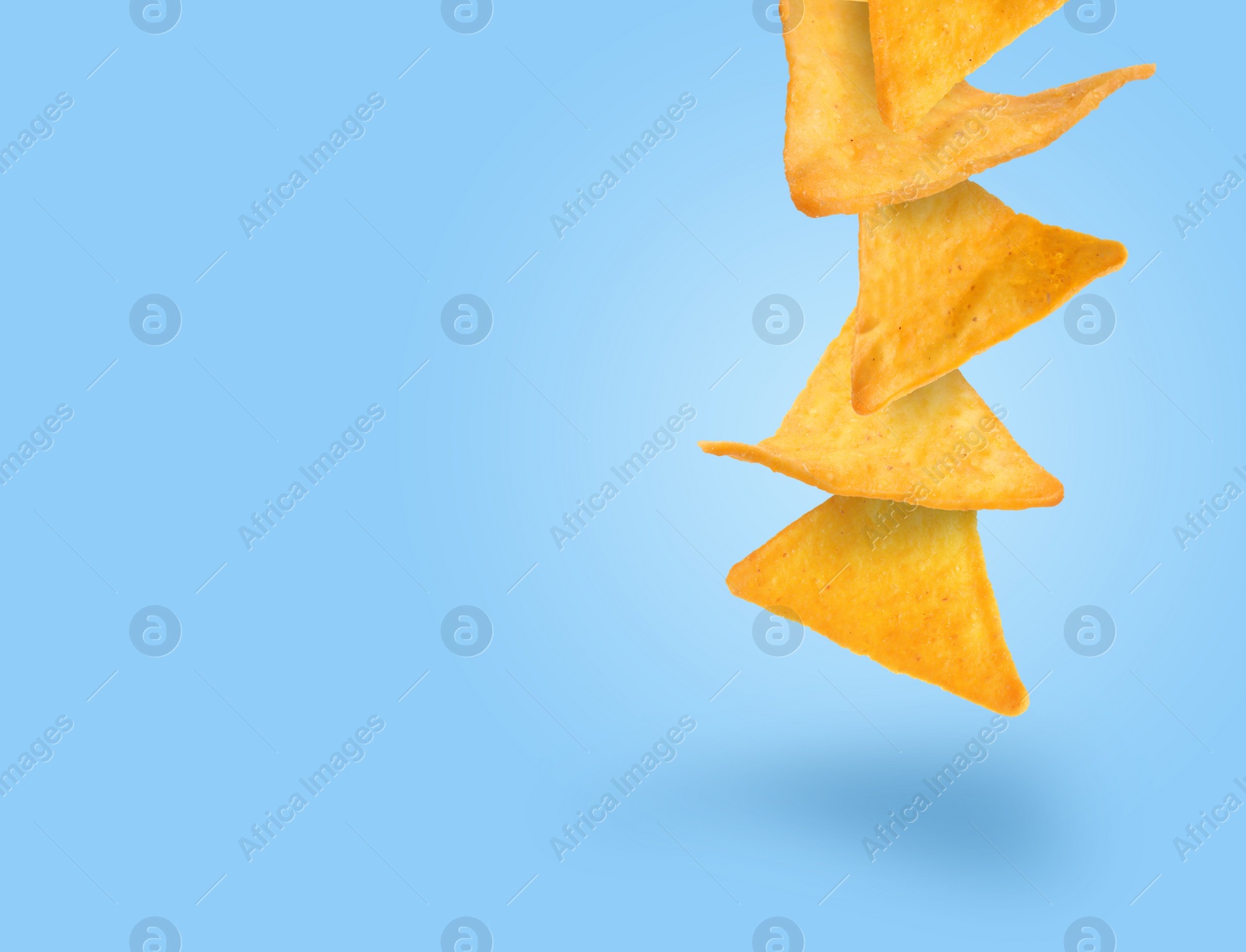 Image of Tasty tortilla chips falling on light blue background, space for text