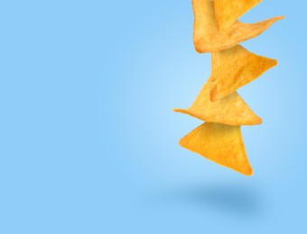 Tasty tortilla chips falling on light blue background, space for text