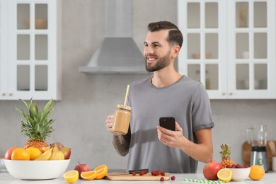 Handsome man with delicious smoothie in kitchen. Space for text