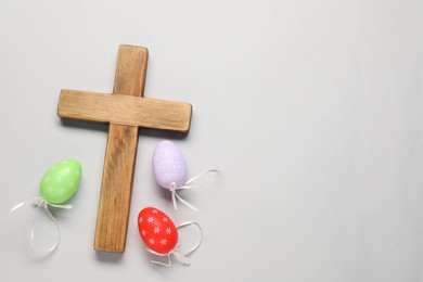 Wooden cross and painted Easter eggs on light grey background, flat lay. Space for text