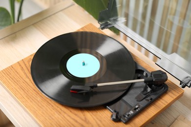 Photo of Stylish turntable with vinyl disc on light wooden table indoors, above view