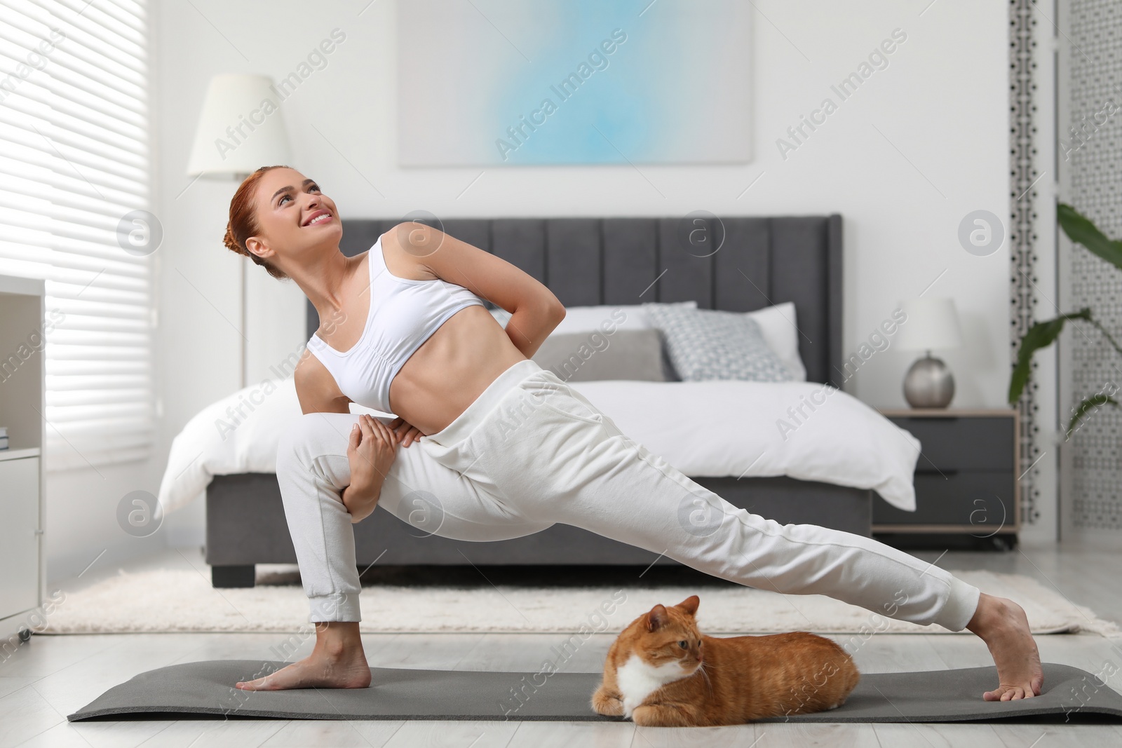 Photo of Beautiful woman with cute red cat practicing yoga on mat at home