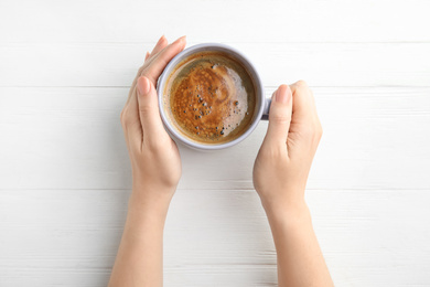 Photo of Woman with cup of coffee at white wooden table, top view