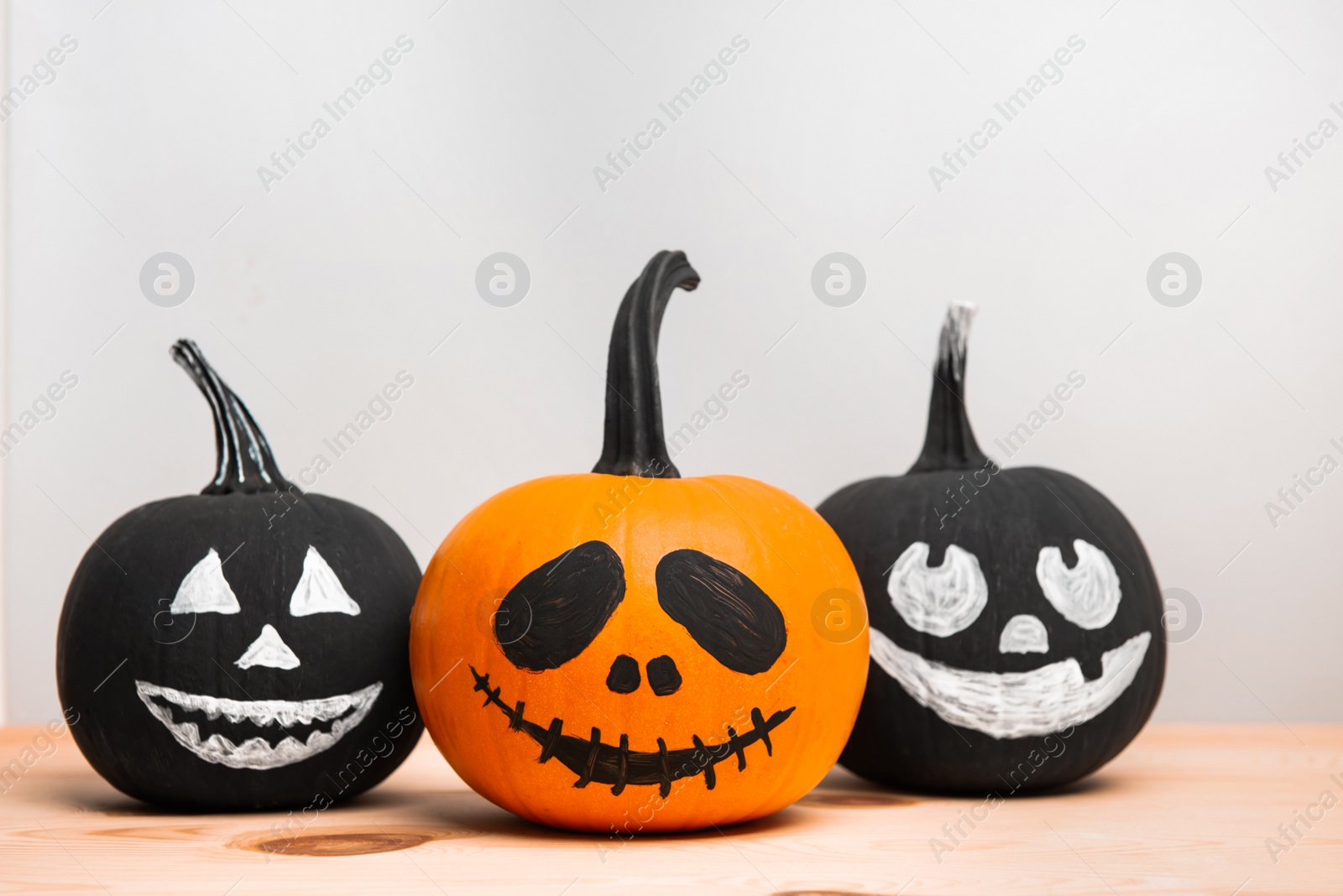 Photo of Halloween celebration. Pumpkins with spooky drawn faces on wooden table, space for text