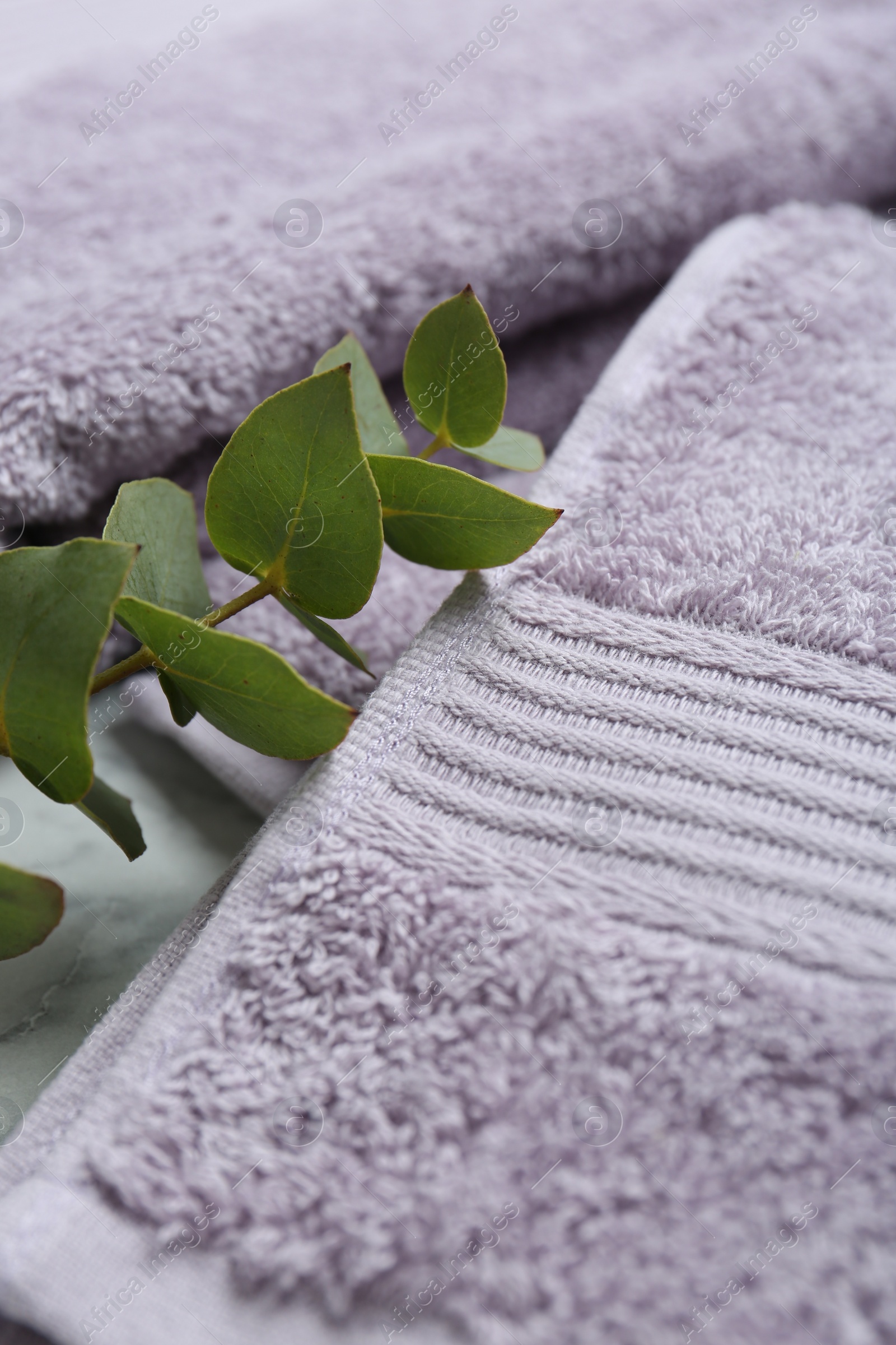 Photo of Violet terry towels and eucalyptus branch on table, closeup