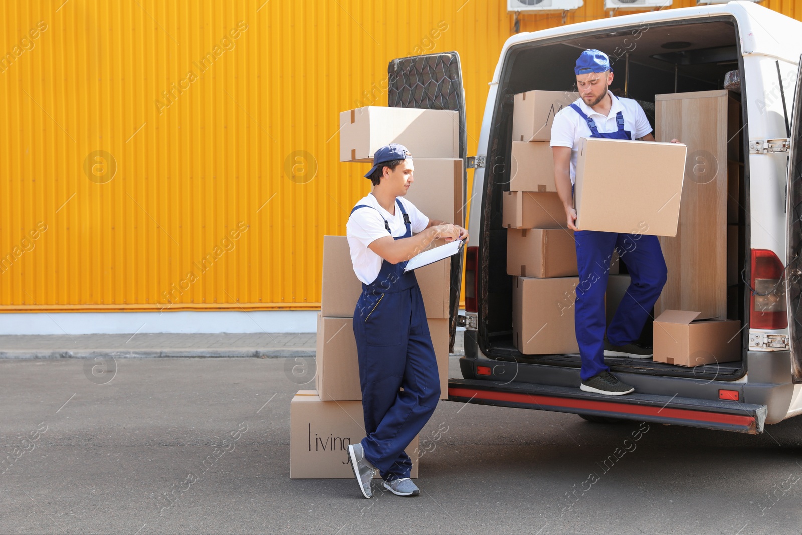 Photo of Male movers unloading boxes from van outdoors