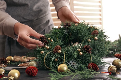 Florist making beautiful Christmas wreath at wooden table indoors, closeup