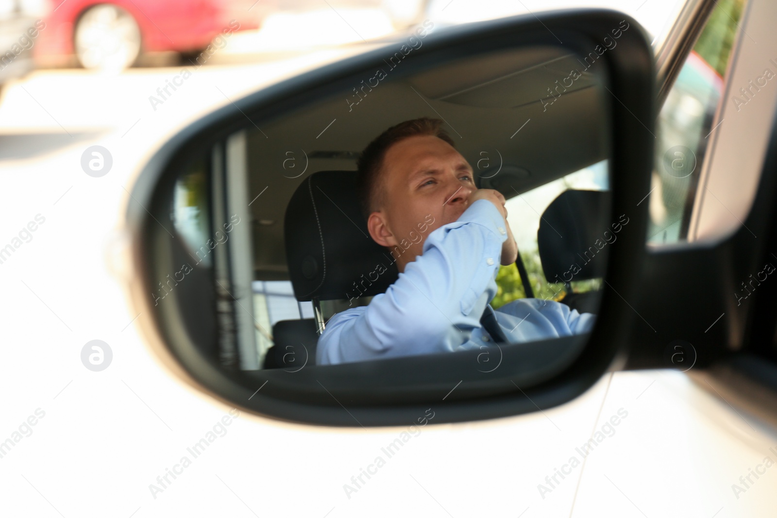 Photo of Tired young man yawning in his auto, view through car side mirror