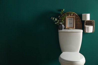Decor elements, paper rolls and toilet bowl near green wall, space for text. Bathroom interior