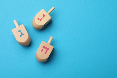 Photo of Wooden dreidels on light blue background, flat lay with space for text. Traditional Hanukkah game