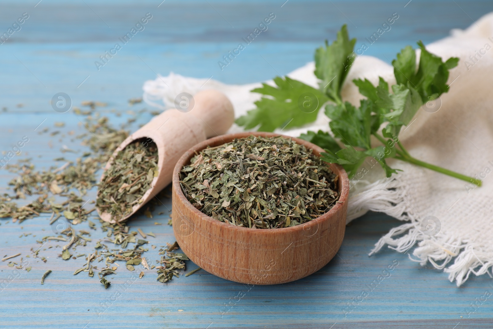 Photo of Dried parsley and fresh leaves on light blue wooden table, closeup