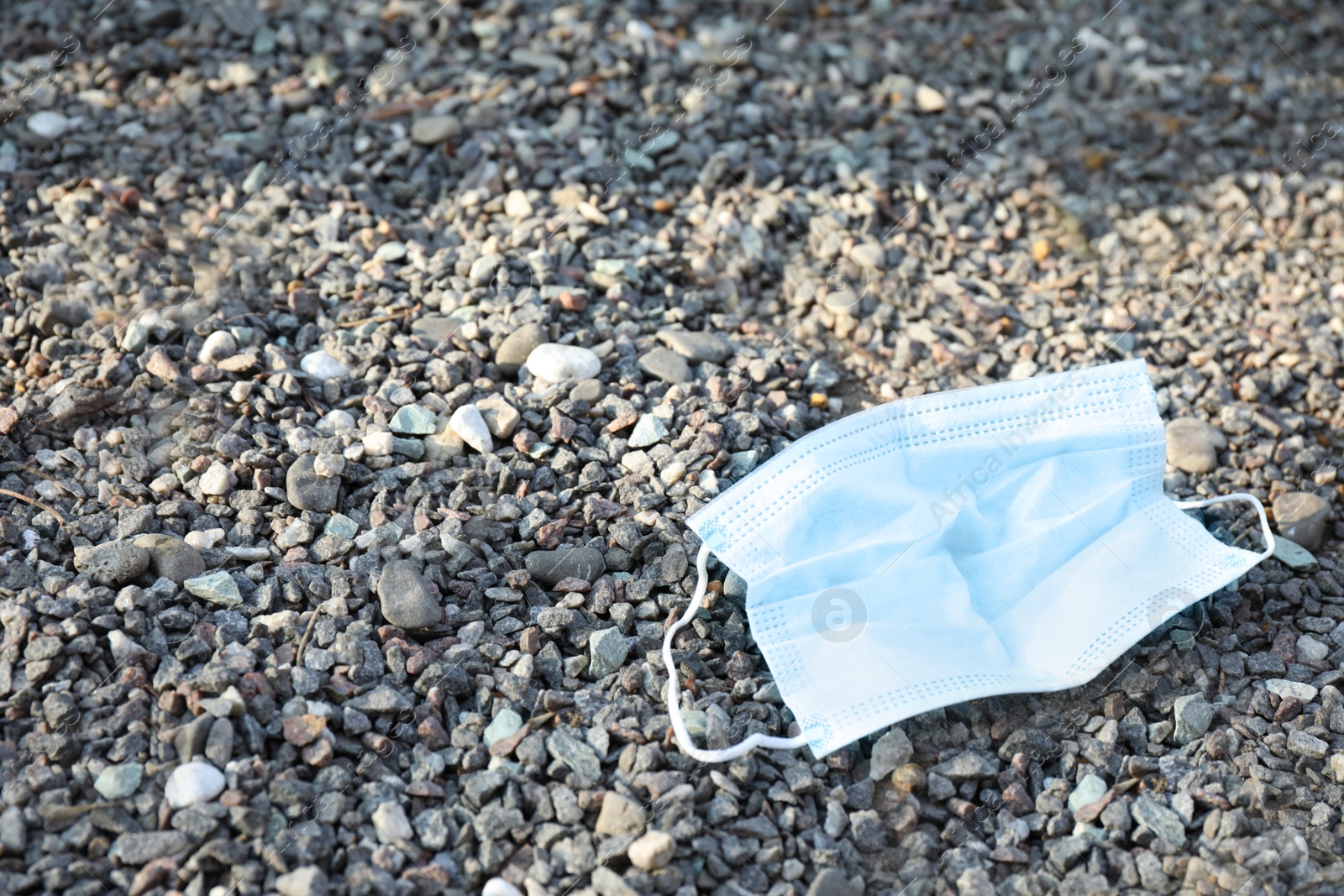 Photo of Used disposable face mask on small pebbles outdoors. Space for text