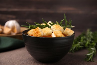 Photo of Delicious crispy croutons and rosemary in bowl on dark table, closeup