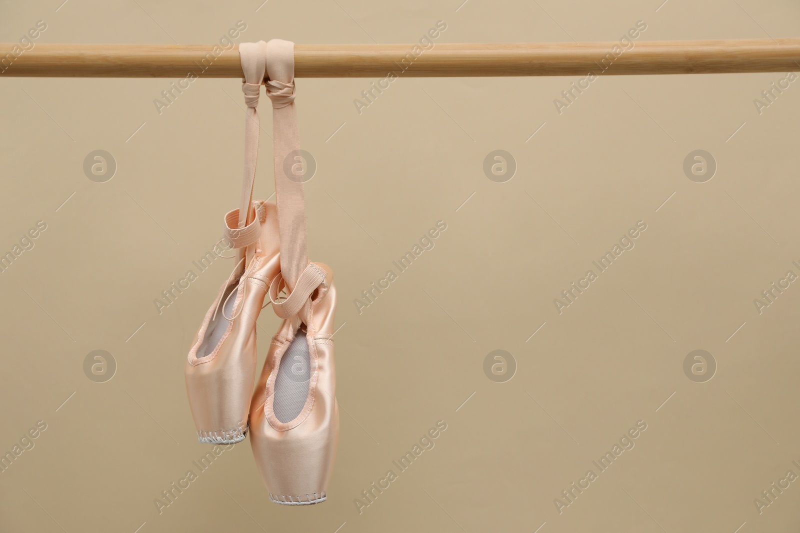 Photo of Elegant pointes hanging on ballet barre against beige background. Space for text