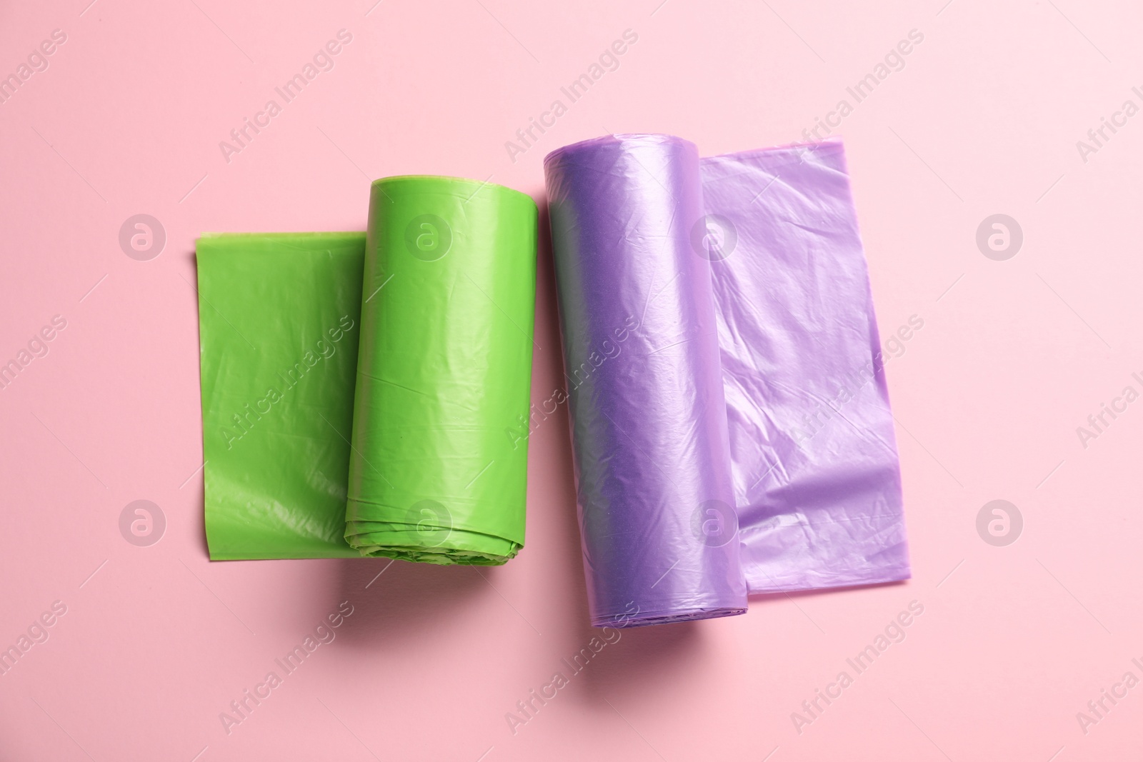 Photo of Rolls of different garbage bags on pink background, flat lay