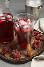 Refreshing hibiscus tea with ice cubes, stick with sugar crystals and roselle petals on grey wooden table