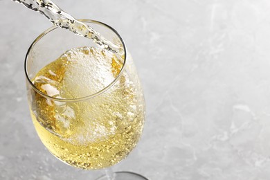 Pouring tasty aromatic wine in glass at gray marble table, closeup. Space for text