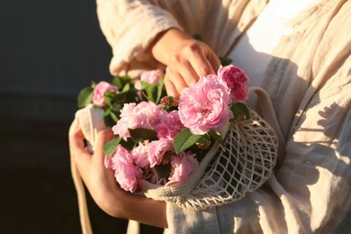 Photo of Woman holding mesh bag with beautiful tea roses outdoors, closeup