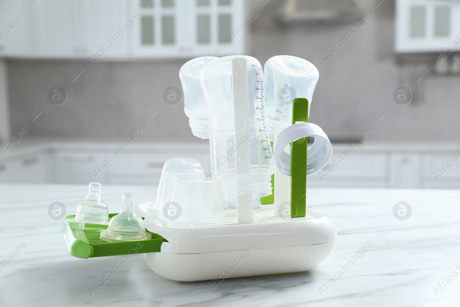 Photo of Dryer with baby bottles and nipples after sterilization on white marble table in kitchen