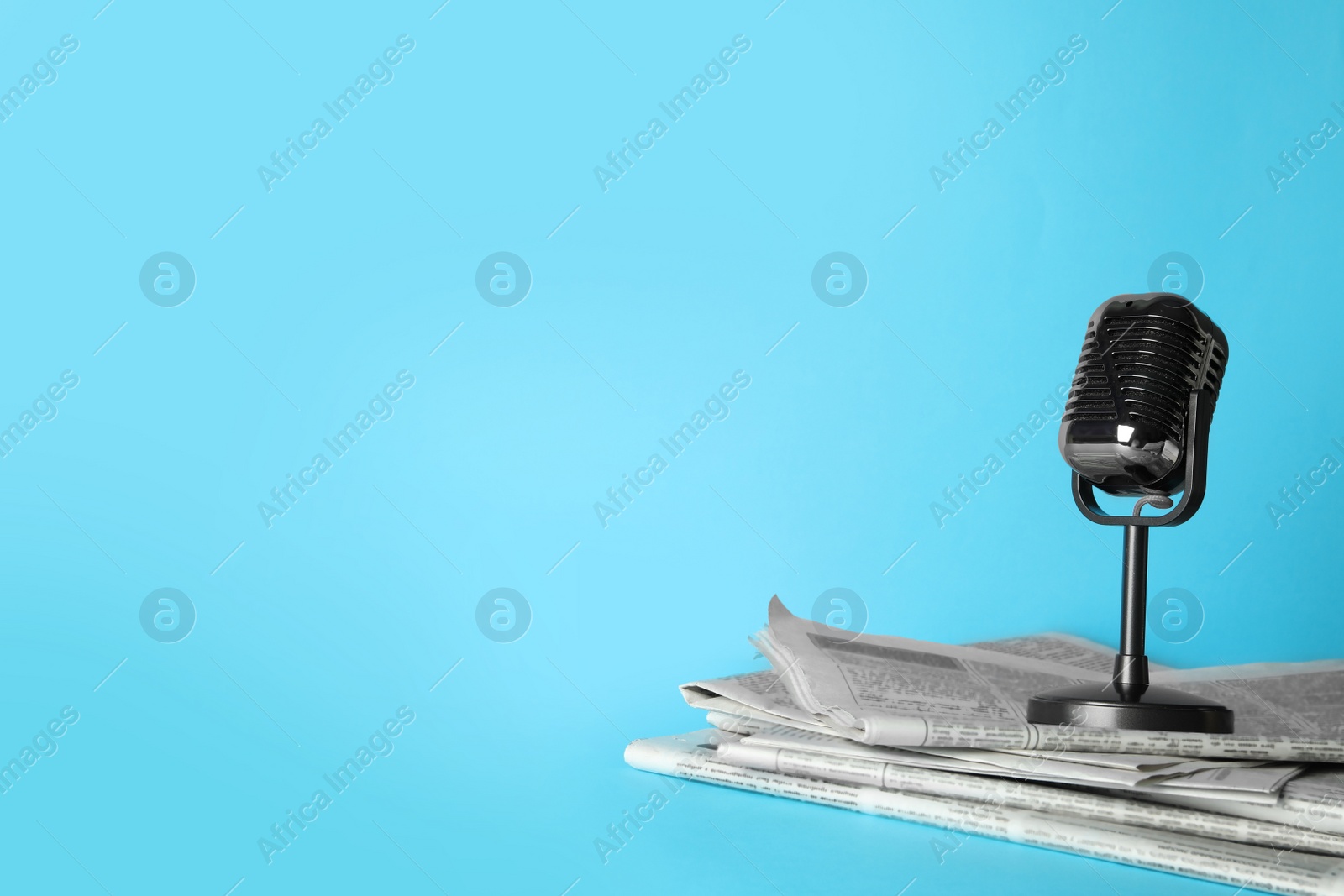 Photo of Newspapers and vintage microphone on light blue background, space for text. Journalist's work