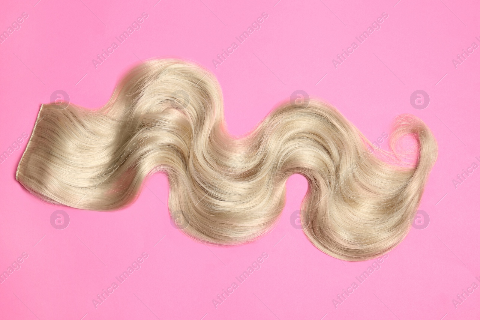 Photo of Lock of blonde wavy hair on color background, top view