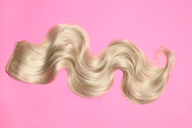 Lock of blonde wavy hair on color background, top view