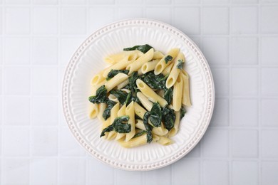 Photo of Tasty pasta with spinach and sauce on white tiled table, top view