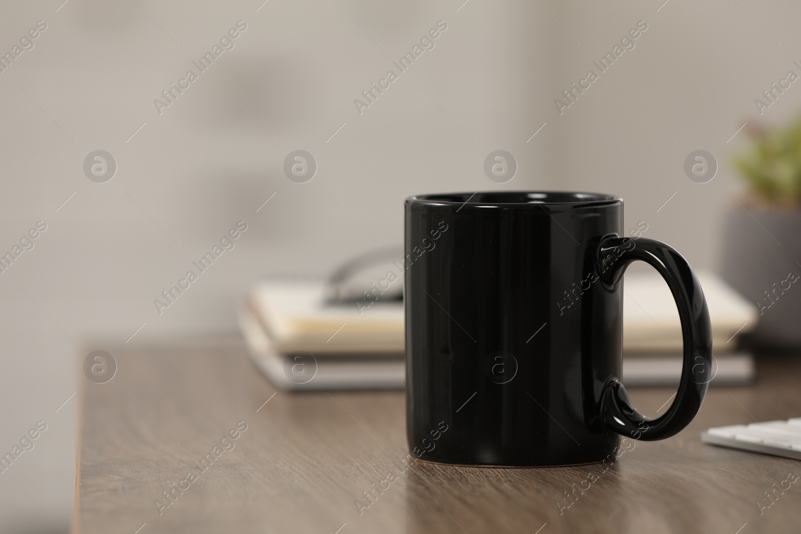 Photo of Black ceramic mug and notebooks on wooden table at workplace. Space for text