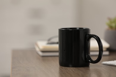 Photo of Black ceramic mug and notebooks on wooden table at workplace. Space for text