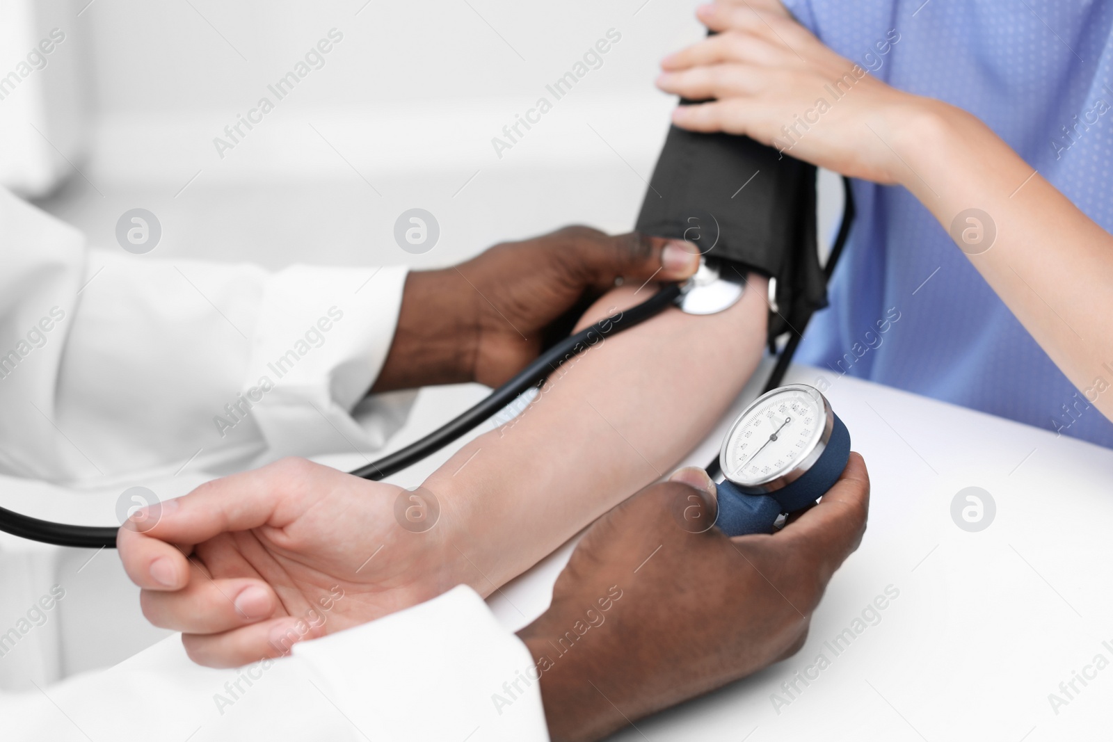 Photo of Young African-American doctor checking patient's pulse and blood pressure in hospital