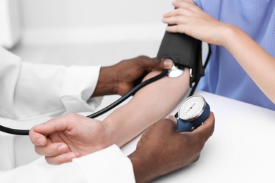 Young African-American doctor checking patient's pulse and blood pressure in hospital