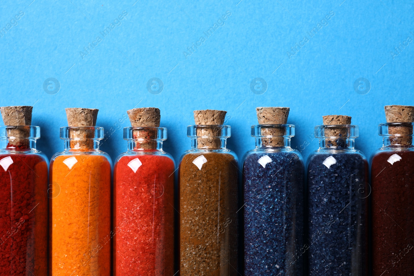 Photo of Glass bottles with different food coloring on light blue background, flat lay. Space for text