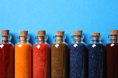 Photo of Glass bottles with different food coloring on light blue background, flat lay. Space for text