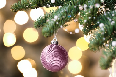 Photo of Pink Christmas ball hanging on fir tree against blurred festive lights